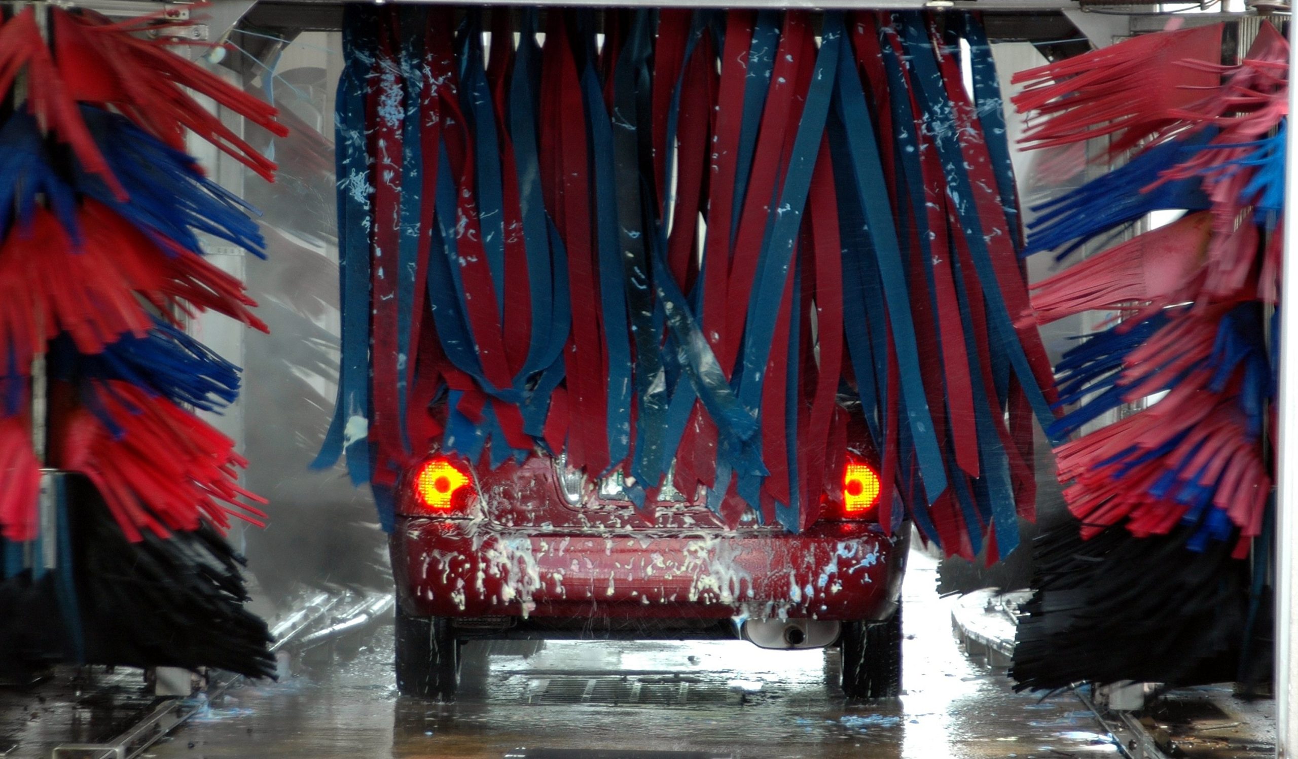 red car inside of an active car wash being washed