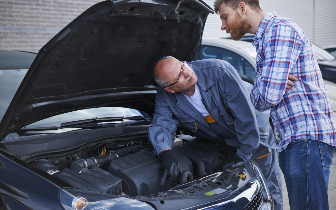 man in overalls by a car engine talking to customer