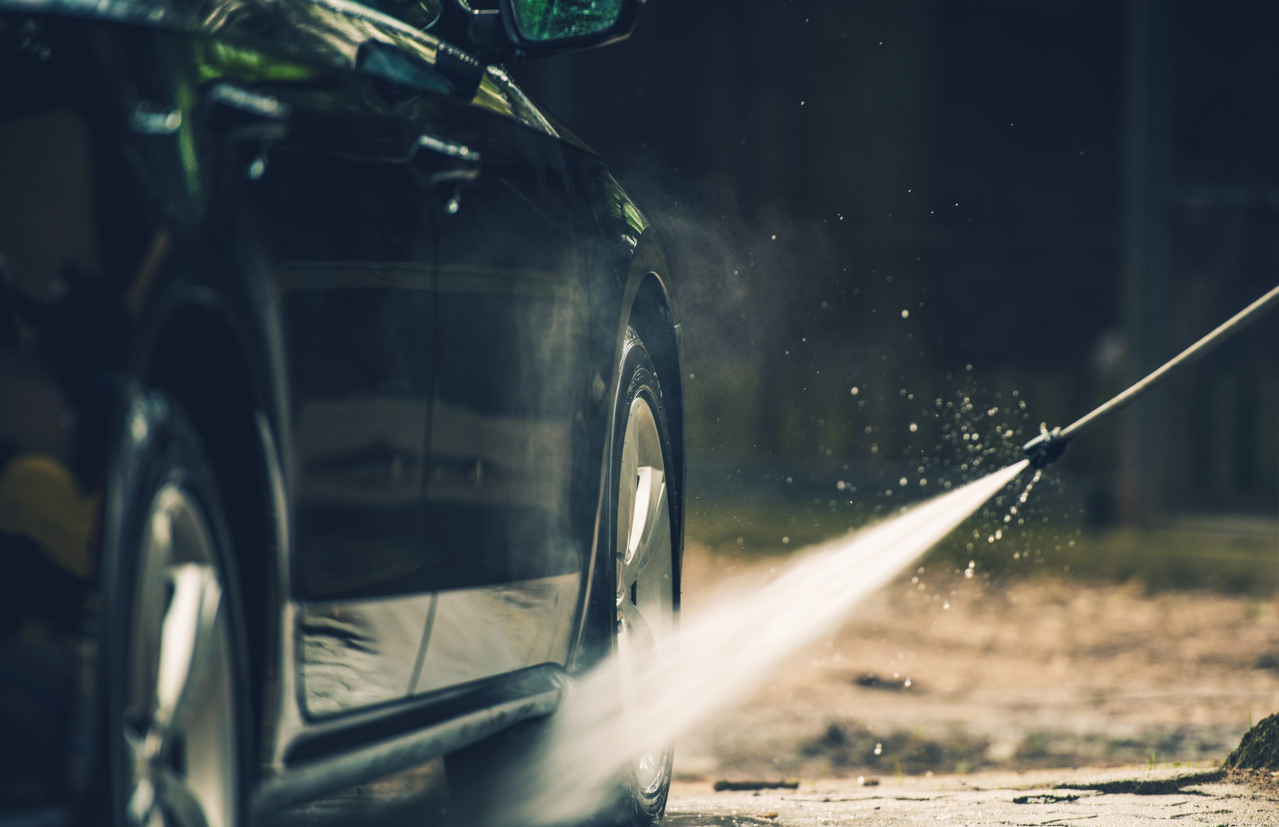 dark car manually being washed with a car wash spraying tool