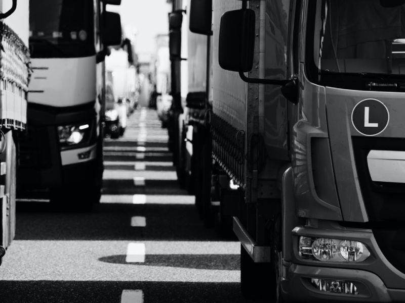 black and white close-up of the front of commercial trucks driving on a congested road